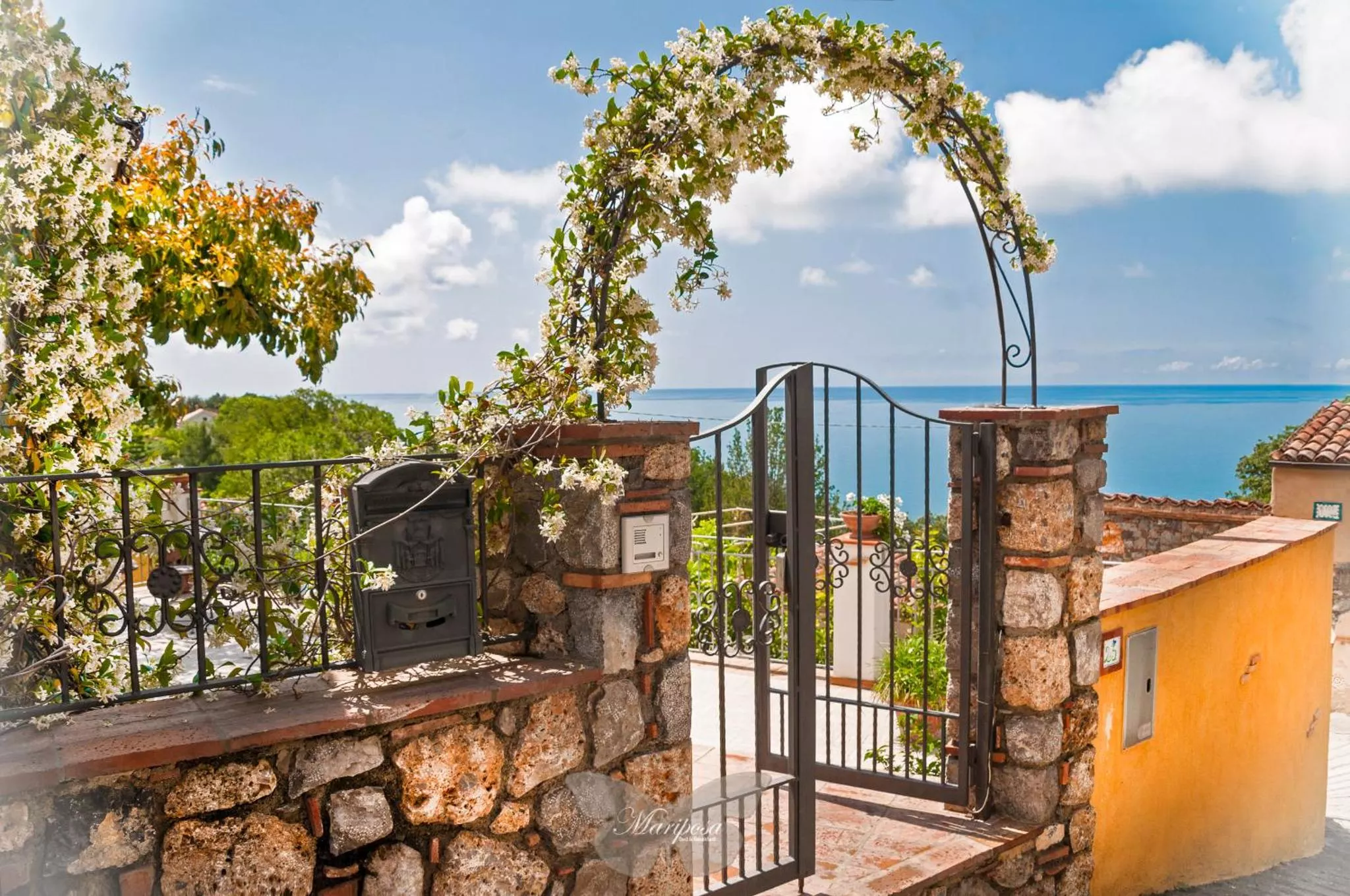 Il cancello d'ingresso del B&B Mariposa con l'arco fiorito e il mare di Cersuta